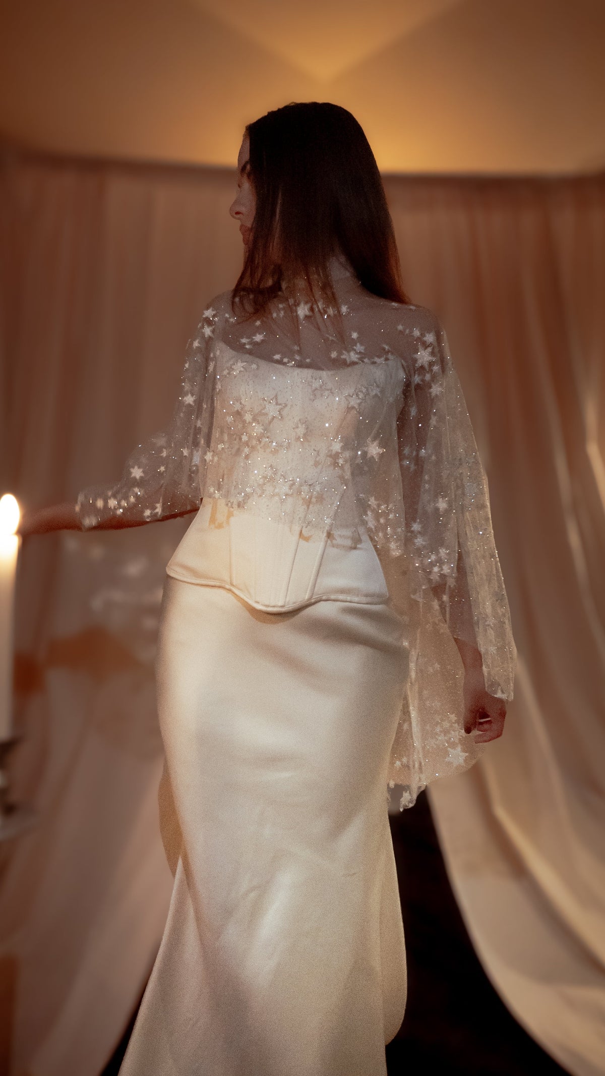 Side view of a bride by candlelight, star tulle bridal cape over a corset top and satin column skirt, Lunar Eclipse Cape Ivory