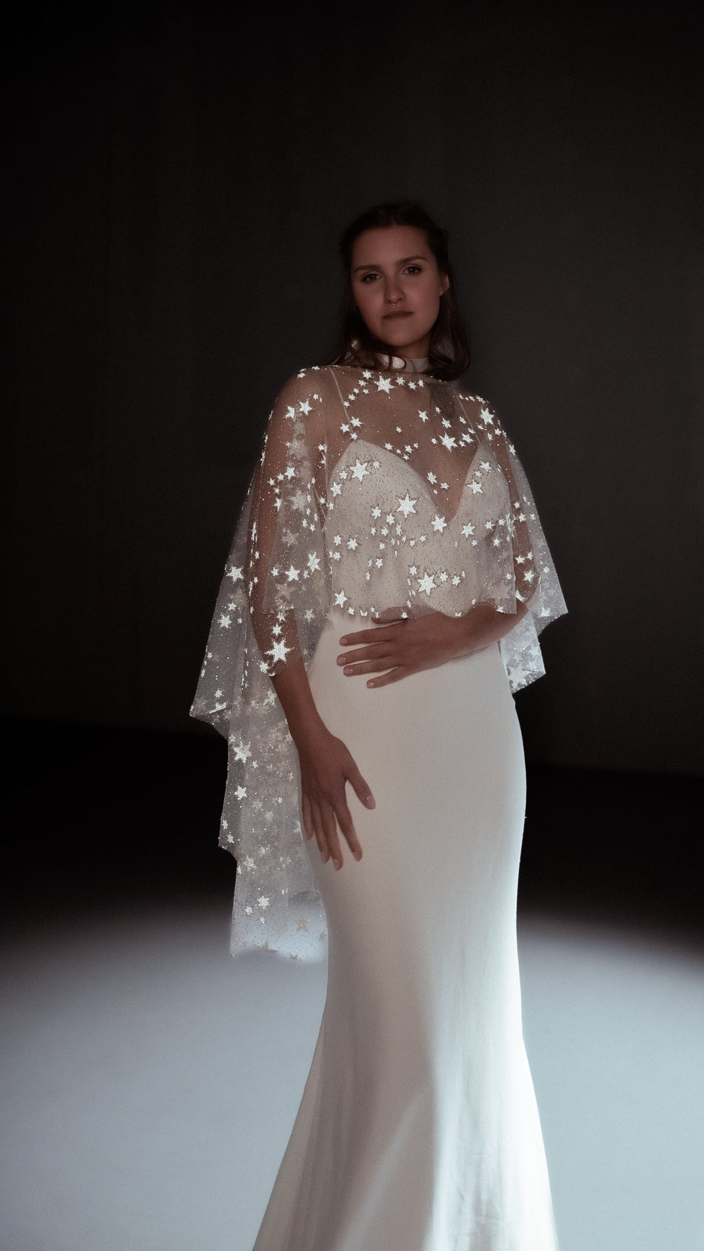 Bride in a studio spotlight wearing an ivory star bridal cape over a strapless mermaid gown, Lunar Eclipse Cape Ivory
