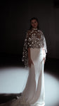 Full-length view of a black star tulle bridal cape for an alt bride, worn over an ivory mermaid gown with a train in a spotlight, Lunar Eclipse Cape Black