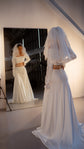 Back view of a voluminous short wedding veil reflected in a studio mirror, bride in a satin two-piece and long gloves, Madonna Veil