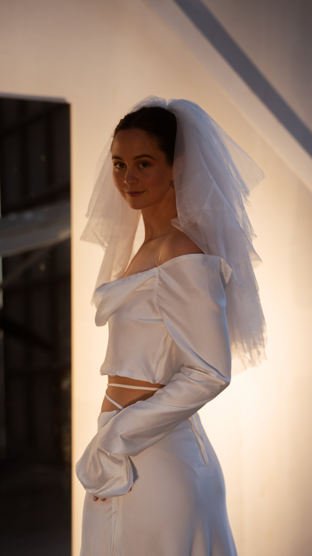 Side view of a short layered wedding veil standing out from the head, off-shoulder satin crop top and long satin gloves, Madonna Veil