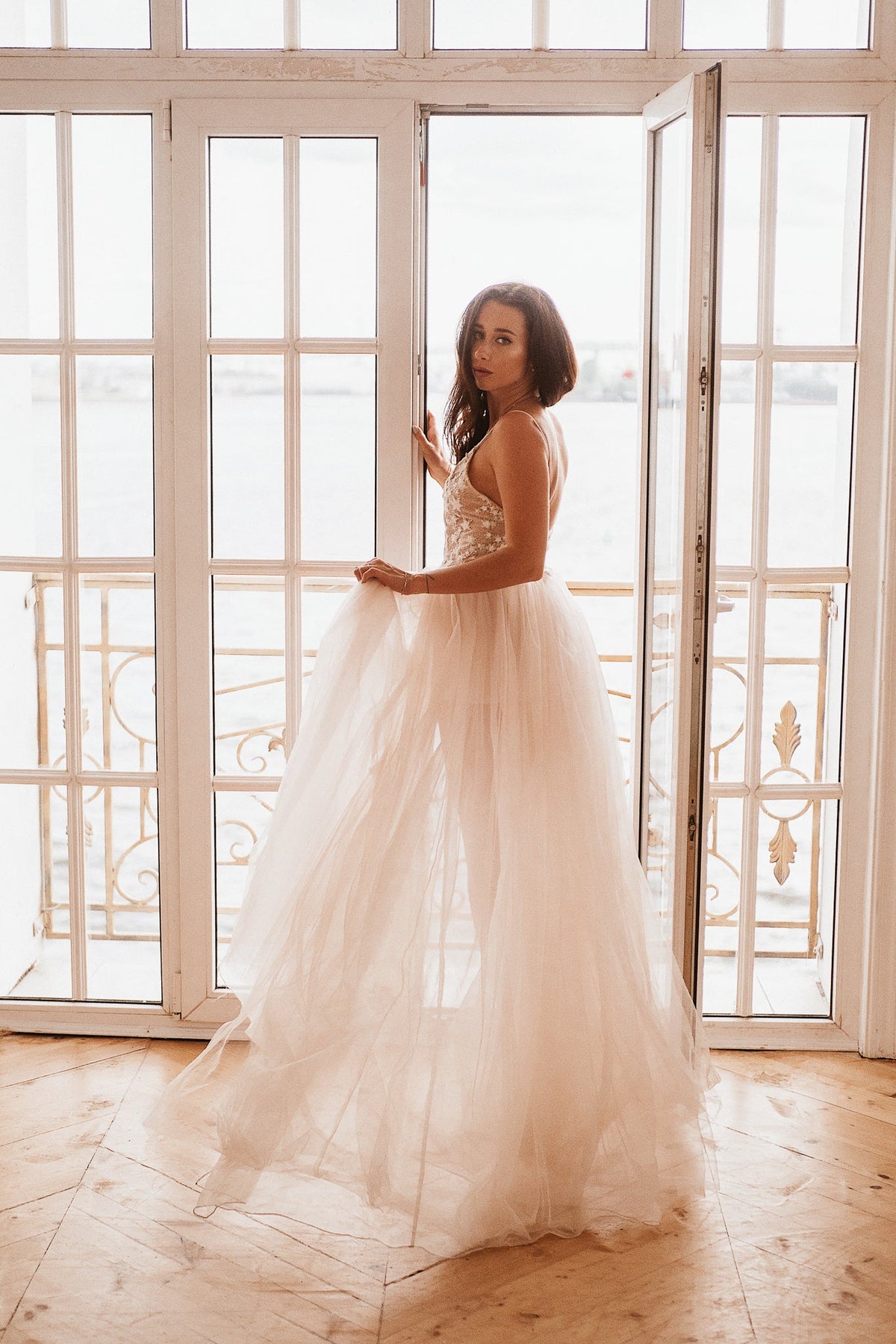 Bride in a doorway of tall glass windows, star corset wedding dress with a full sheer skirt and pooled hem, Make a Wish