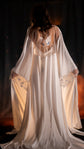 Back view of a celestial bridal robe in ivory satin with a sheer back, embroidered blue butterfly and star cuffs, long train. Metamorphosis Robe by Ephemeris