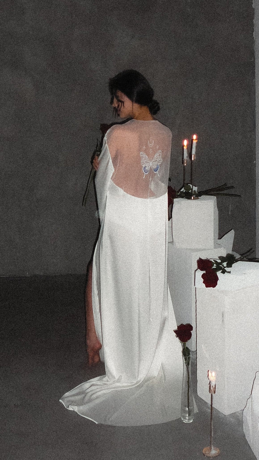 Back view in low light of a satin bridal robe with a sheer back panel and butterfly embroidery, train on concrete, Metamorphosis Robe