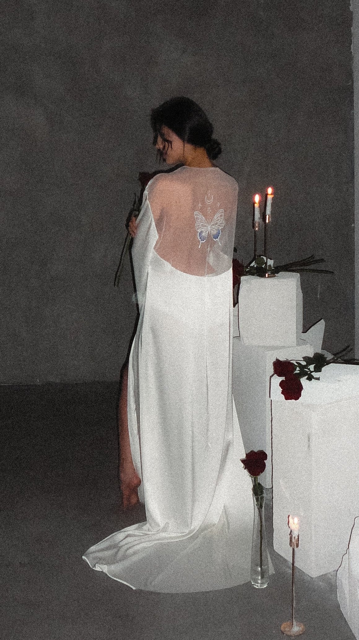 Back view in low light of a satin bridal robe with a sheer back panel and butterfly embroidery, train on concrete, Metamorphosis Robe