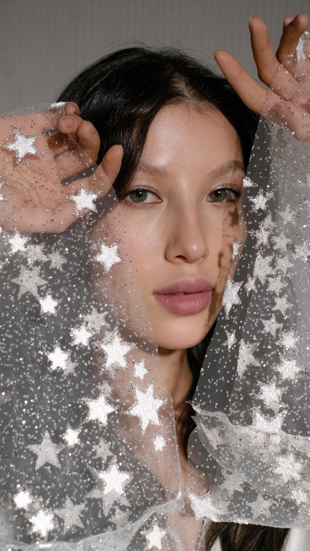 Close portrait framed by sparkling star tulle sleeves raised to the face, ivory bridal robe, Metamorphosis Robe