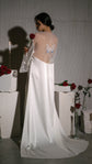 Rear view of a long satin bridal robe with a sheer butterfly back panel, rose in hand, candles and plinths, Metamorphosis Robe