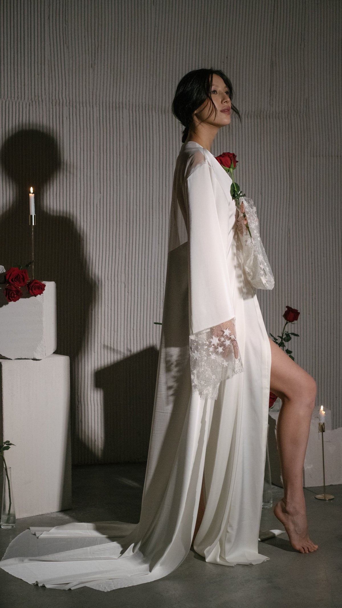 Side profile of a barefoot bride in a floor-length satin bridal robe with lace star cuffs and a pooled train, Metamorphosis Robe
