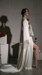Side profile of a barefoot bride in a floor-length satin bridal robe with lace star cuffs and a pooled train, Metamorphosis Robe