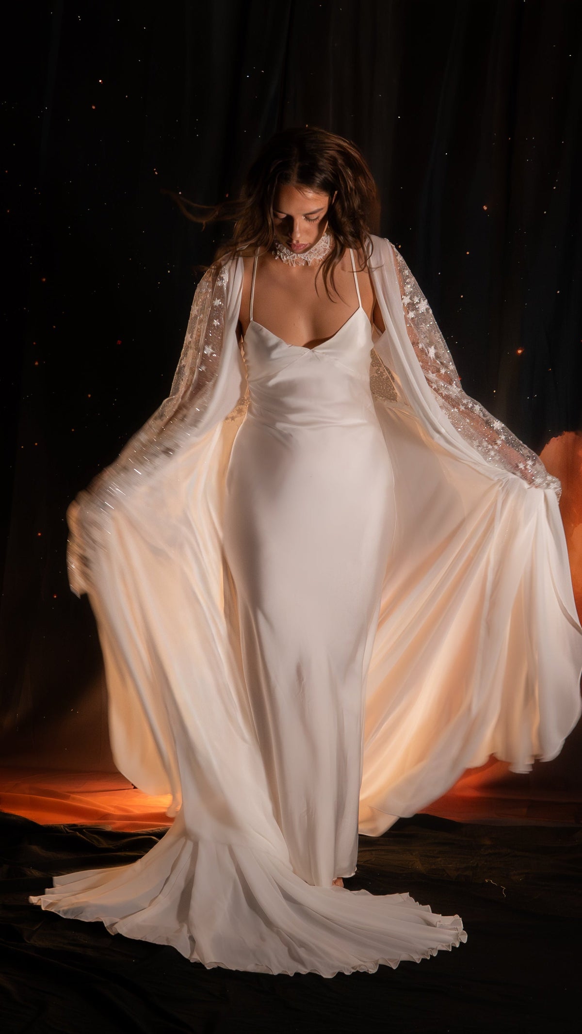 Bride holding open a satin bridal robe with sheer star sleeves over a long slip dress, lace choker, dark starry set, Metamorphosis Robe