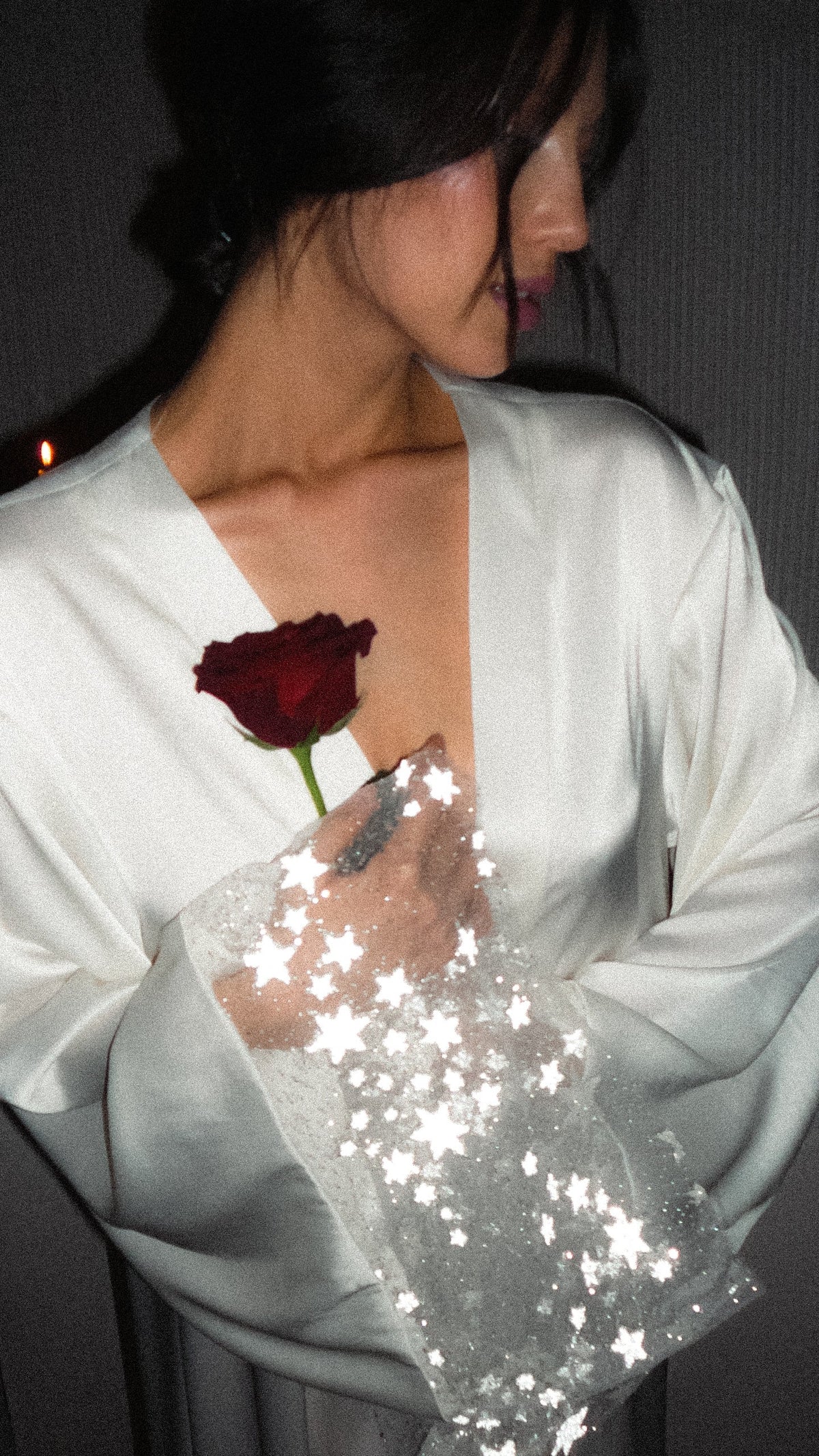Bride looking down in a wrap satin bridal robe with wide star tulle cuffs, holding a single red rose, Metamorphosis Robe