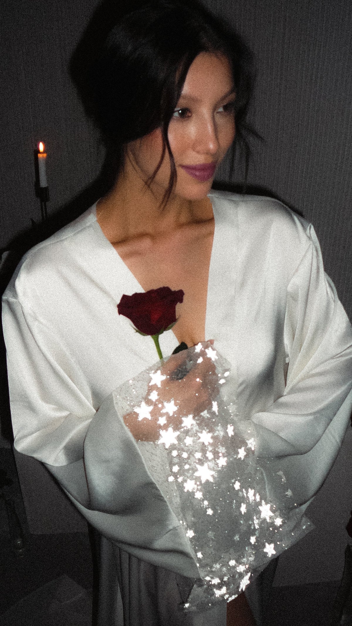 Waist-up shot of a smiling bride in a V-neck satin bridal robe, starry tulle sleeve and red rose close to the lens, Metamorphosis Robe