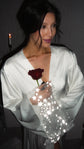 Waist-up shot of a smiling bride in a V-neck satin bridal robe, starry tulle sleeve and red rose close to the lens, Metamorphosis Robe