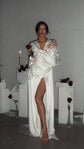 Bride wrapping her arms in long star tulle sleeves, satin bridal robe falling open at the leg, roses and candles, Metamorphosis Robe