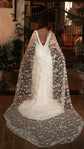 Back view of a bride in a star-scattered bridal cape and low-back ivory gown at an evening garden gate, Milky Way Cape