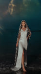 Bride in a V-neck slip dress standing in shallow water under a star wedding veil, large moon behind her, Milky Way Veil