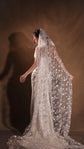 Bride holding out the edges of a star-scattered wedding veil, back three-quarter view in a warm studio, Milky Way Veil