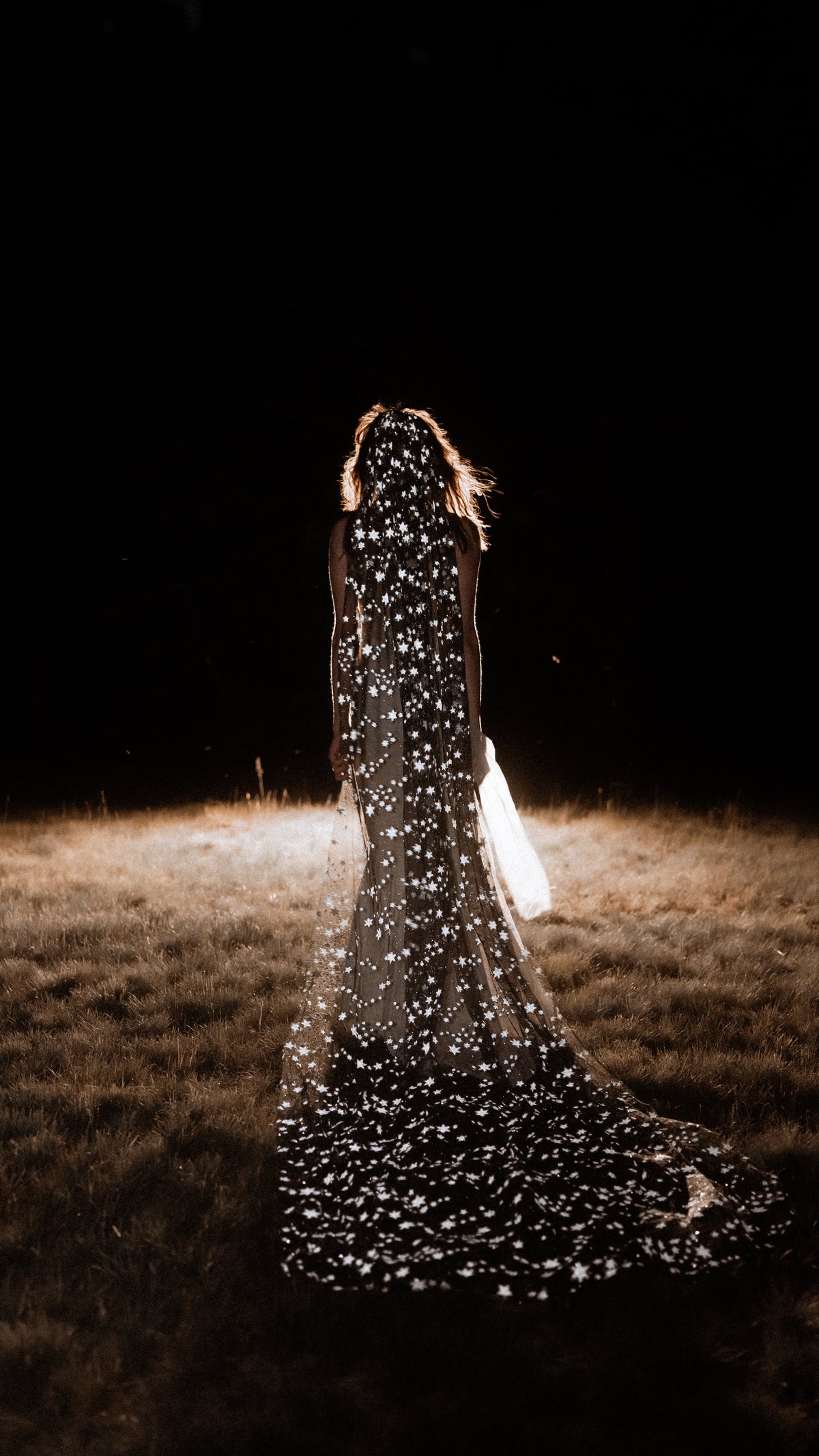 Black star wedding veil trailing across a dark field at night, stars catching the light, back view, Milky Way Veil Black by Ephemeris