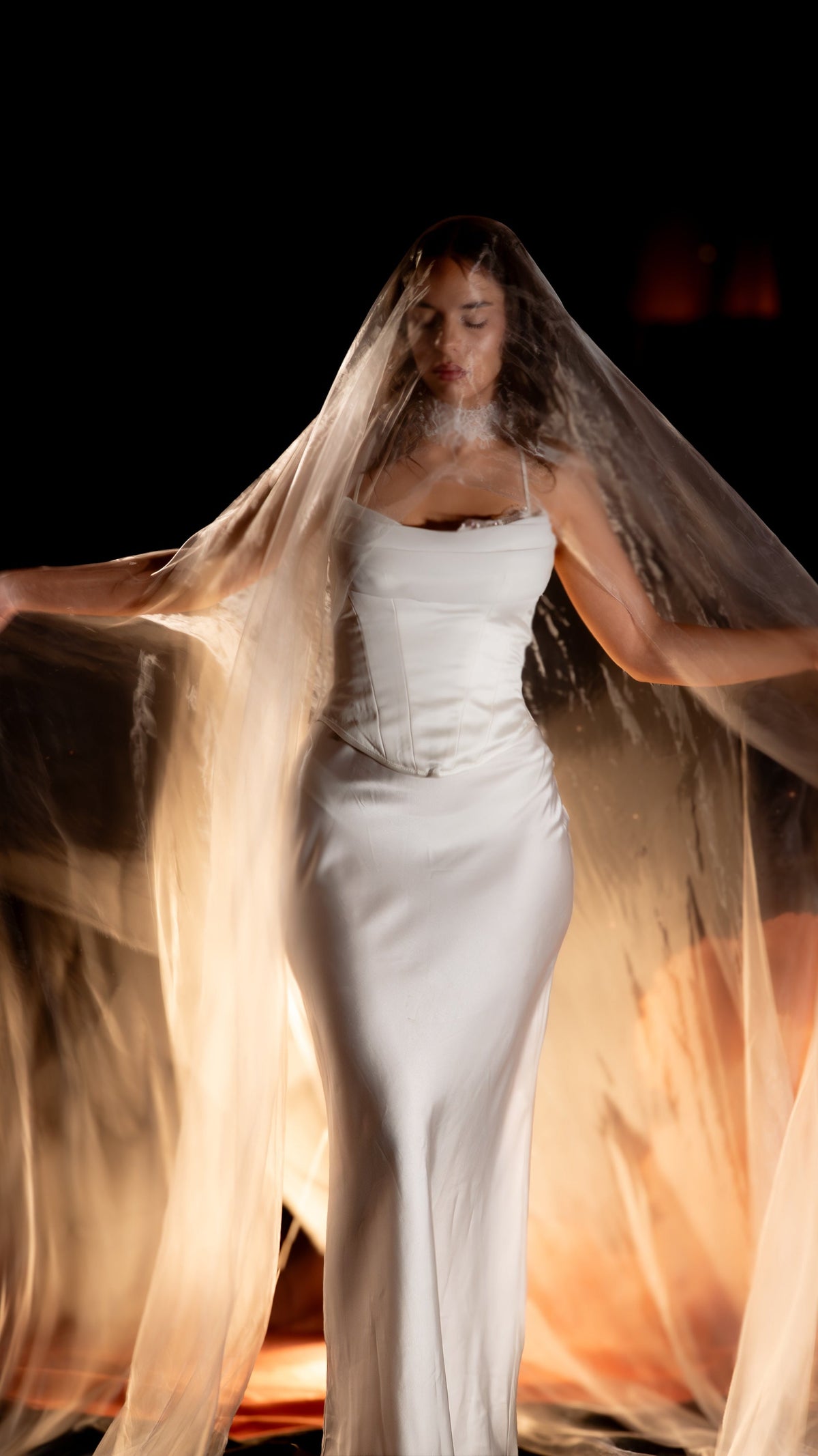 Bride with closed eyes under the Moonglade super organza veil, worn over her face and spread wide by her hands, lit warm gold from behind. Mantilla wedding veil by Ephemeris.