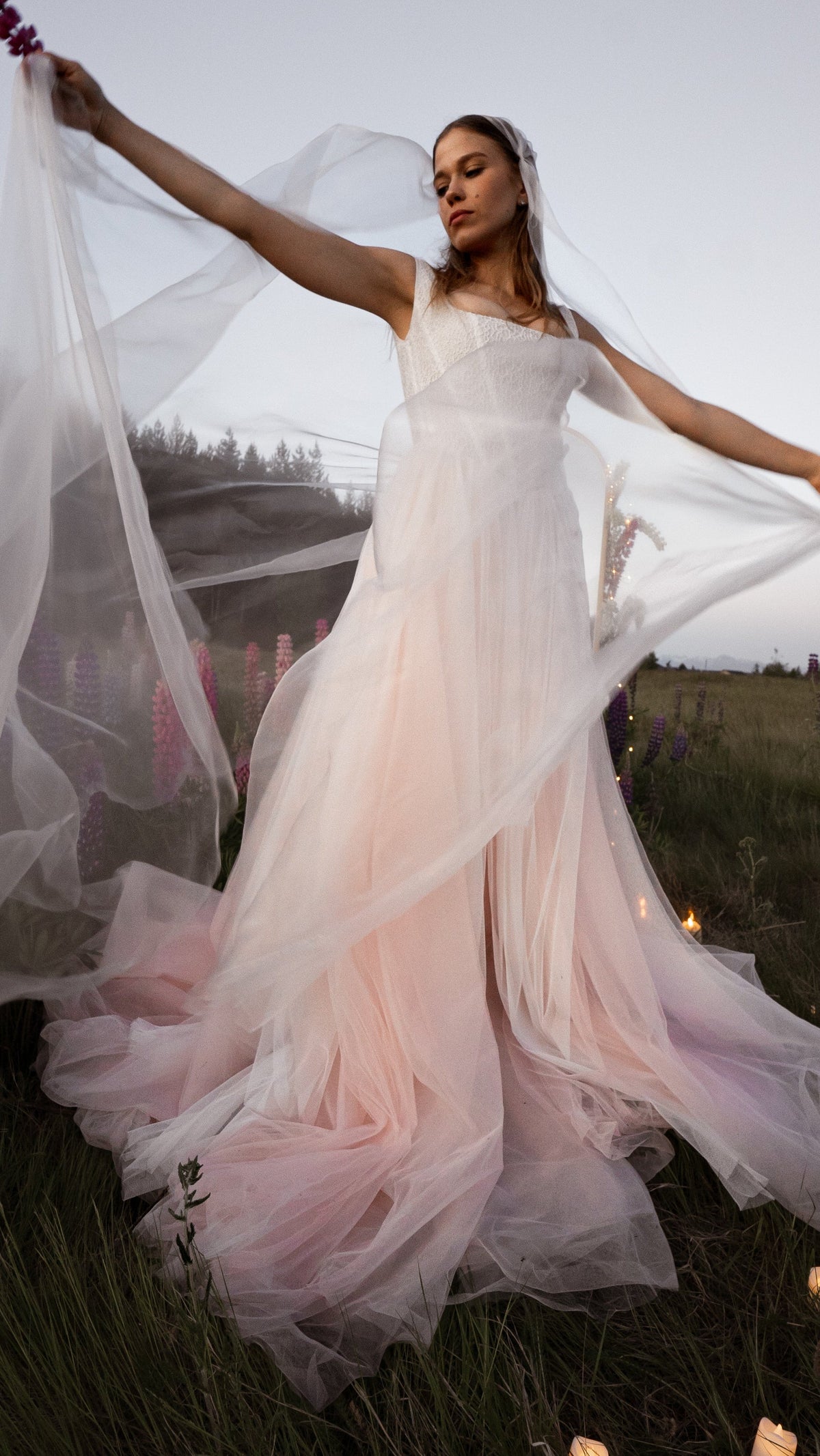 Bride spreading a sheer super organza mantilla veil wide in a lupine meadow at dusk, Moonglade wedding veil