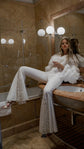Petal-sleeve bridal jacket worn off the shoulder with Sun Flares trousers, bride posing on a marble bathroom vanity, My Darling Hurricane