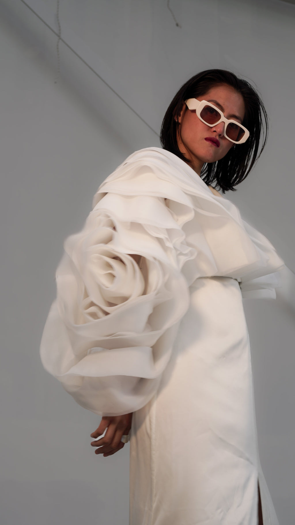 Editorial close-up of a flower-bud organza sleeve on an ivory bridal jacket, model in white sunglasses, My Darling Hurricane