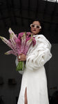 Bridal jacket with layered petal sleeves over a white slit dress, model holding pink lupines and wearing sunglasses, My Darling Hurricane