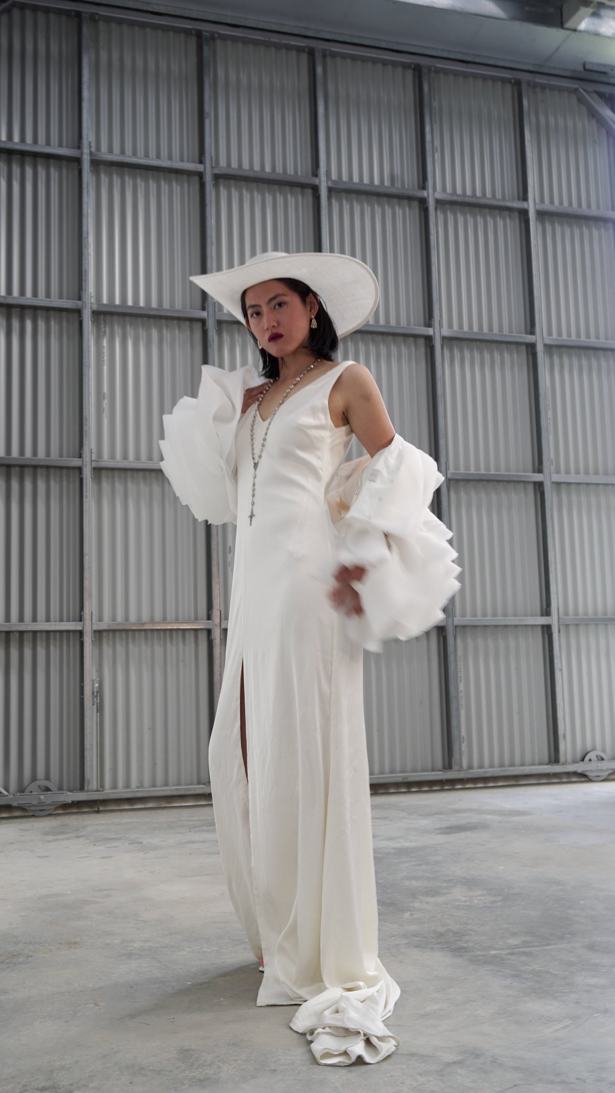 Full-length look with a petal bridal jacket slipping off the shoulders over a long V-neck slip dress, wide hat, warehouse, My Darling Hurricane
