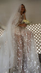 Cathedral wedding veil in soft plain tulle over a bride in a sheer star gown, seated with a bouquet by a lattice wall, Niagara Veil by Ephemeris