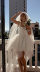 Bride shading her eyes on a sunny balcony, plain cathedral wedding veil framing a corset mini dress and bouquet, Niagara Veil