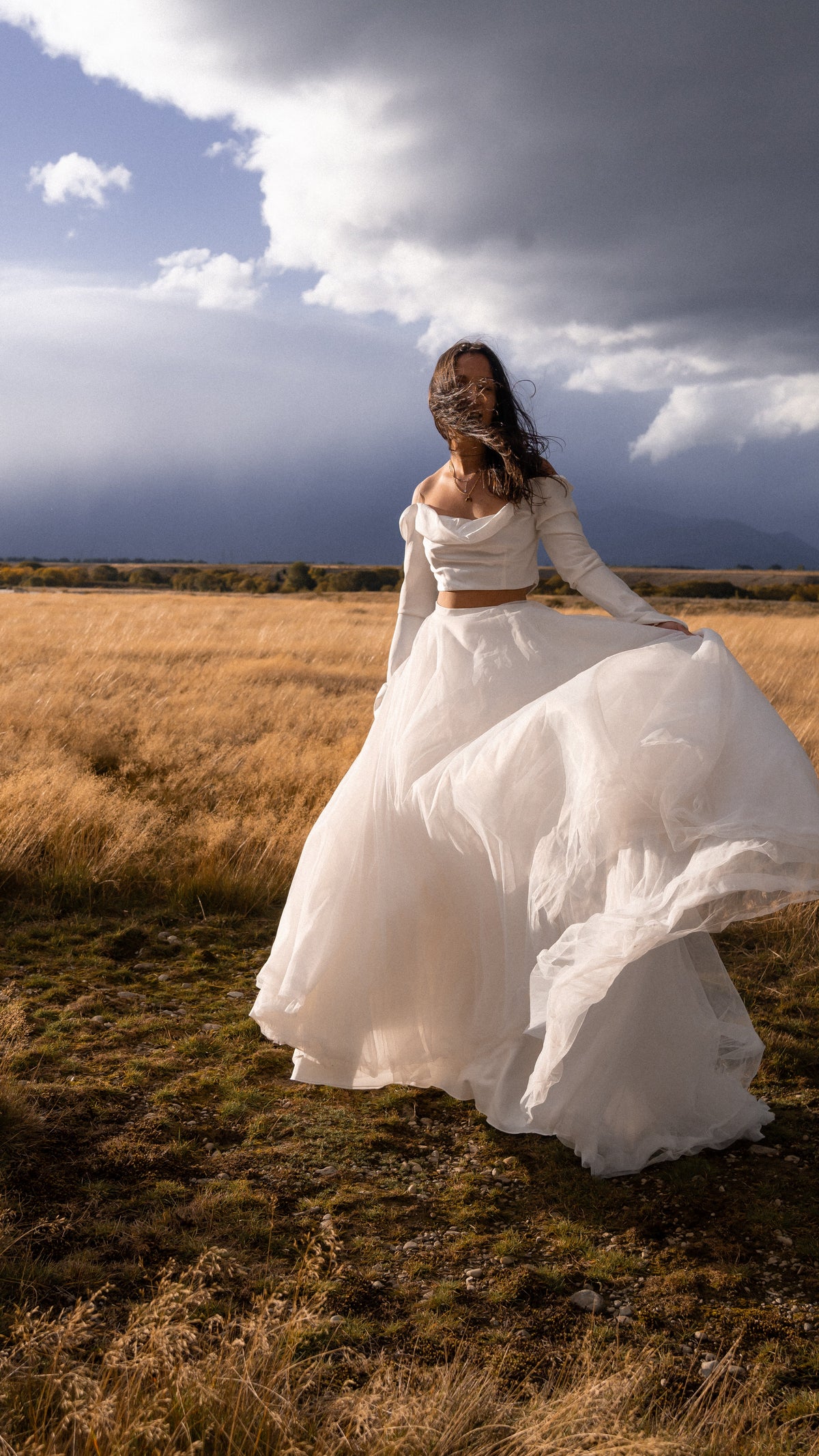 Tulle bridal skirt swirling in the wind with a long-sleeve crop top, golden grass field under storm clouds, Olivia Skirt by Ephemeris