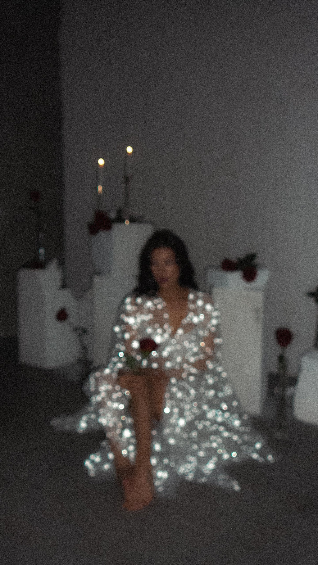 Blurred candlelit shot of a model seated in a sparkling star bridal robe holding a rose, Orion Robe