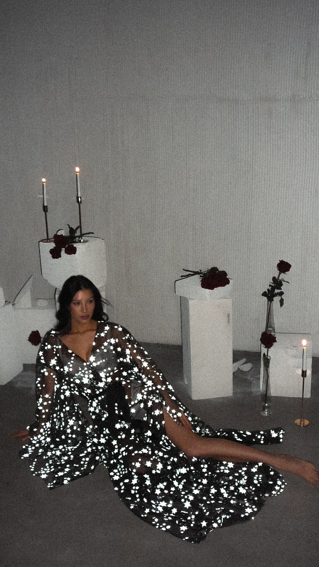 Starry bridal robe flashing bright against a dark floor, model seated with legs stretched out among candles, Orion Robe