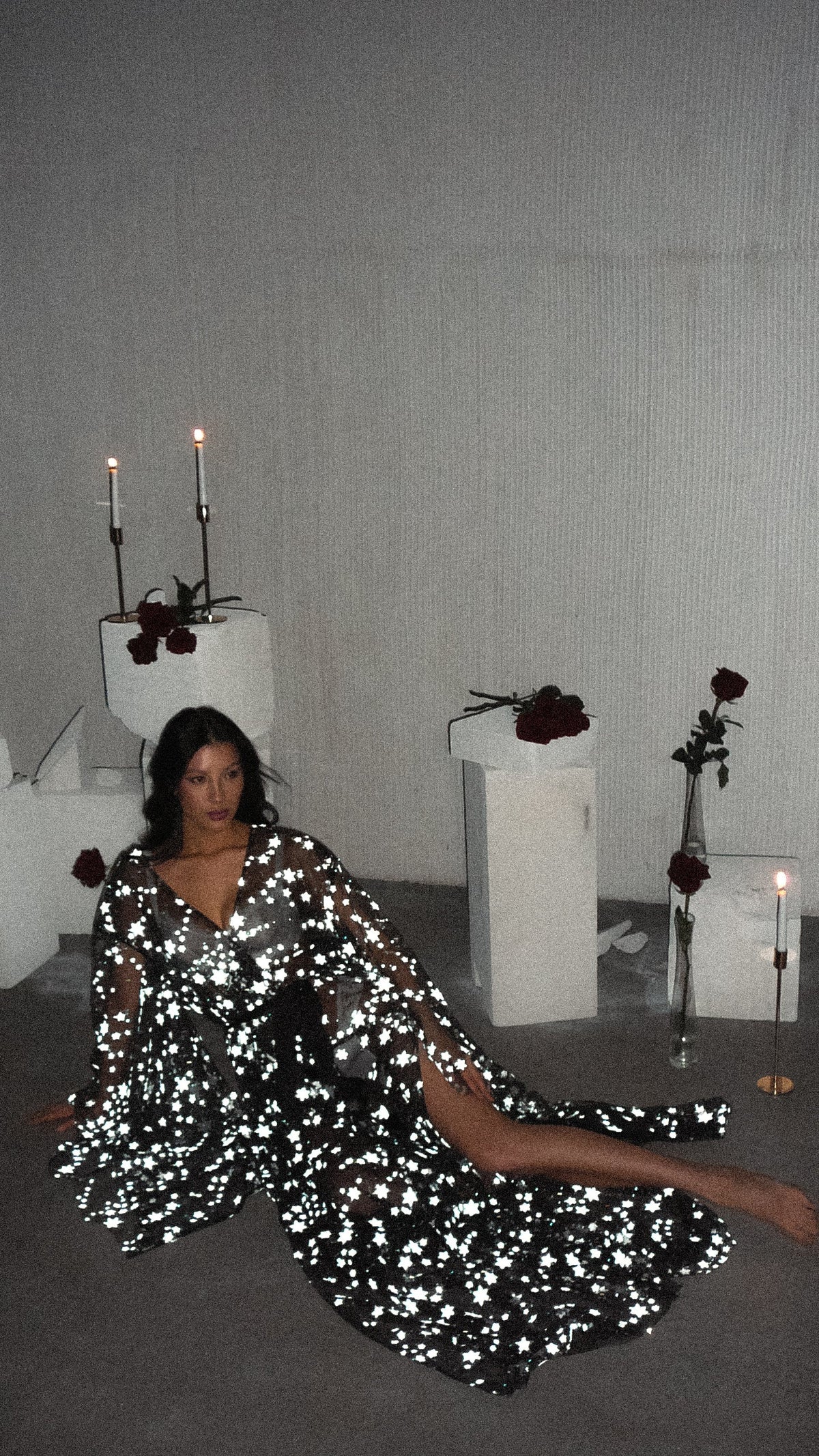 Starry bridal robe flashing bright against a dark floor, model seated with legs stretched out among candles, Orion Robe