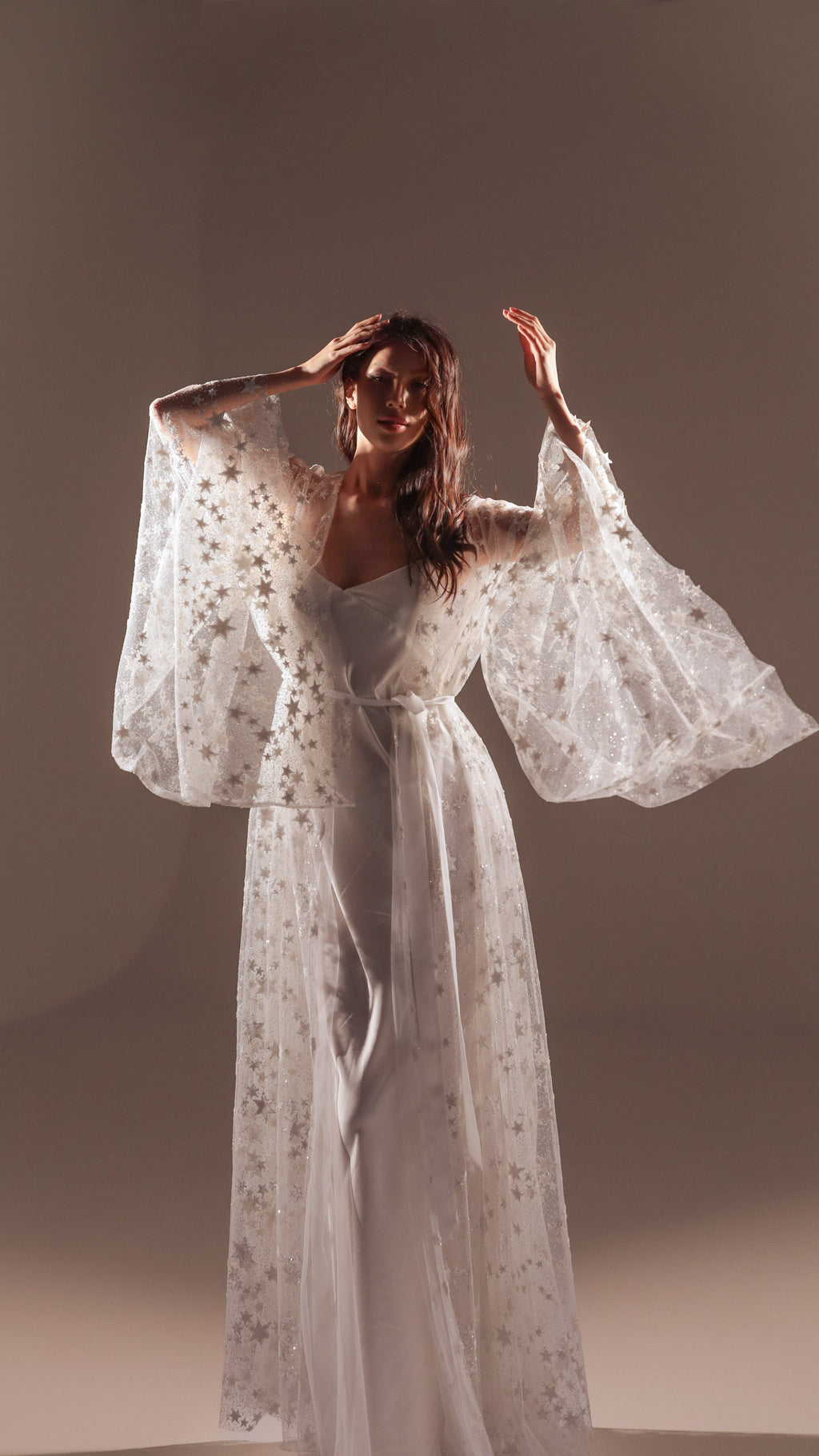 Model with arms raised in a long star tulle bridal robe over a white slip dress, soft studio light, Orion Robe