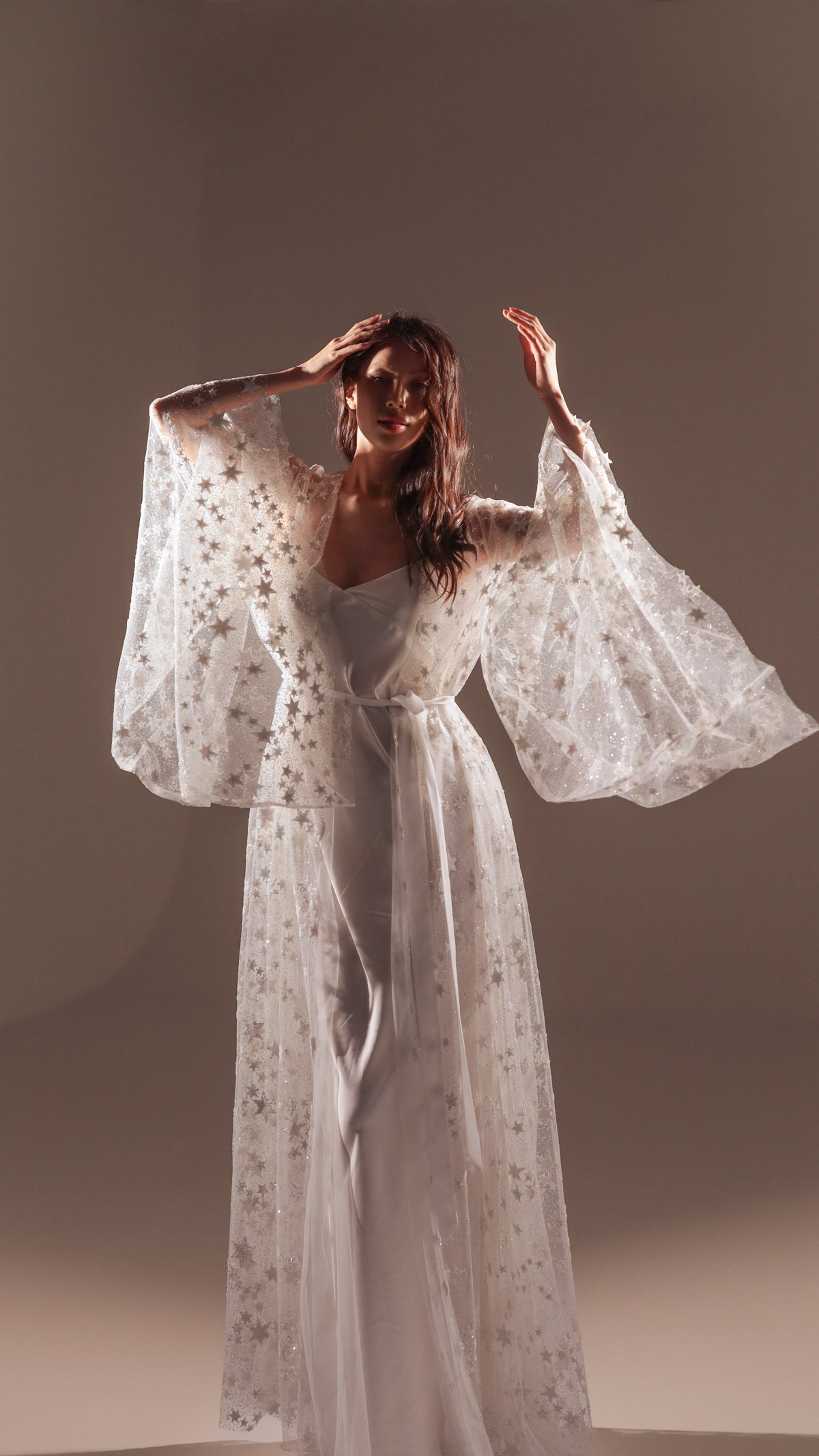 Model with arms raised in a long star tulle bridal robe over a white slip dress, soft studio light, Orion Robe