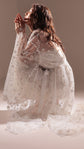 Model kneeling in profile in a star tulle bridal robe with a ribbon tie, hands raised to her face, Orion Robe