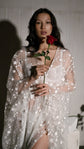 Model holding a red rose against a sheer star bridal robe worn over white lingerie, ribbed wall behind, Orion Robe