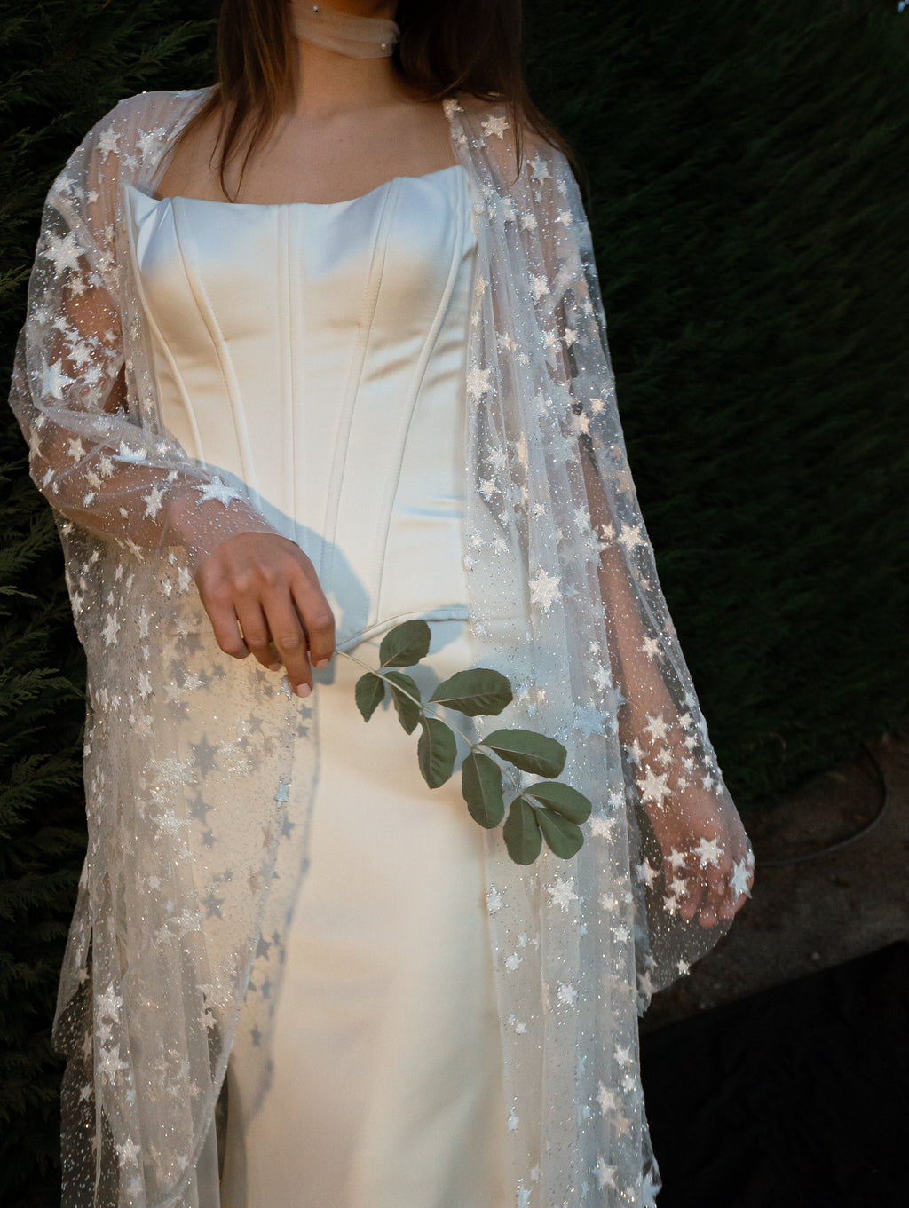 Sheer bridal robe with scattered stars draped over an ivory satin corset dress, hand holding greenery, Orion Robe