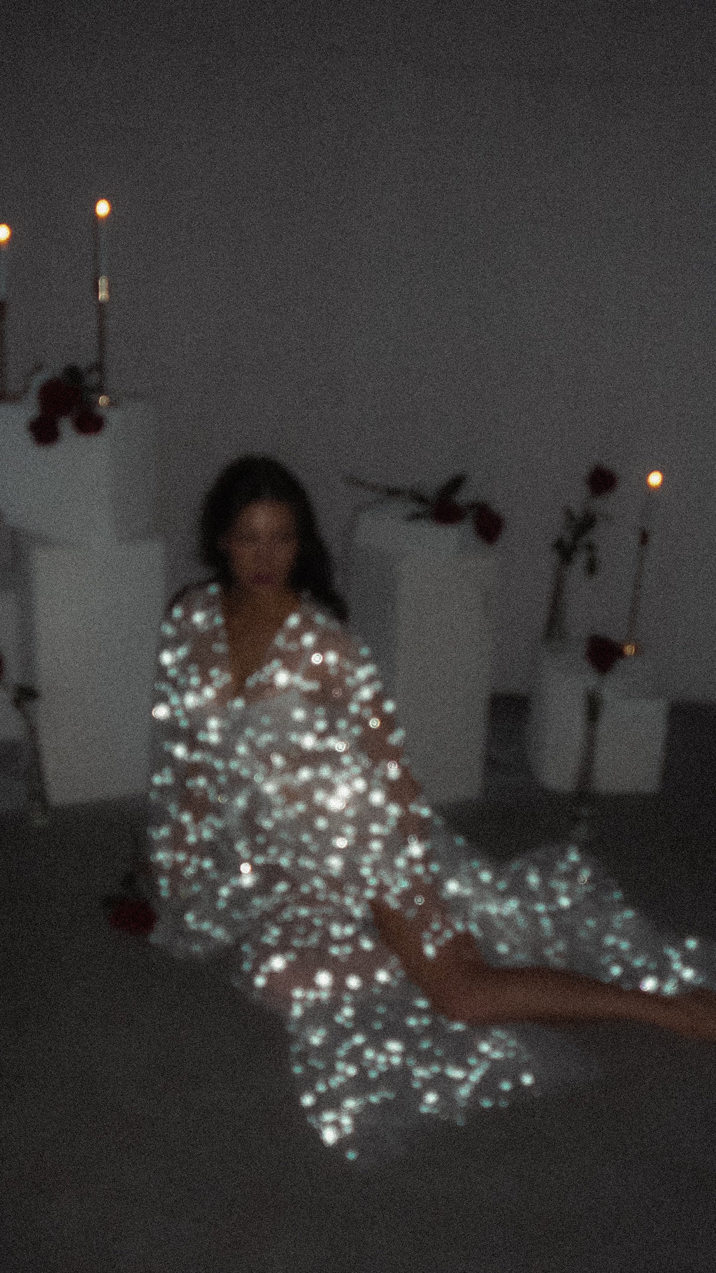 Soft-focus shot of a model lounging on the floor in a starry bridal robe, candles and roses in the background, Orion Robe
