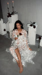 Model sitting on the floor holding a red rose in a sheer starry bridal robe, candles and plinths behind, Orion Robe Black