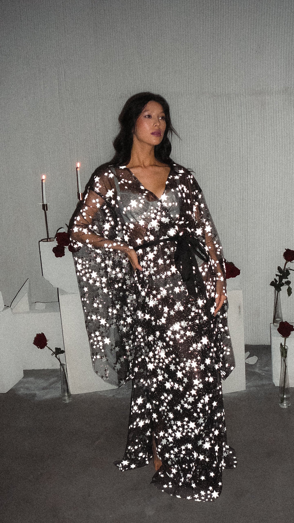 Black star bridal robe tied at the waist, model with hand on hip among candles and roses, Orion Robe Black