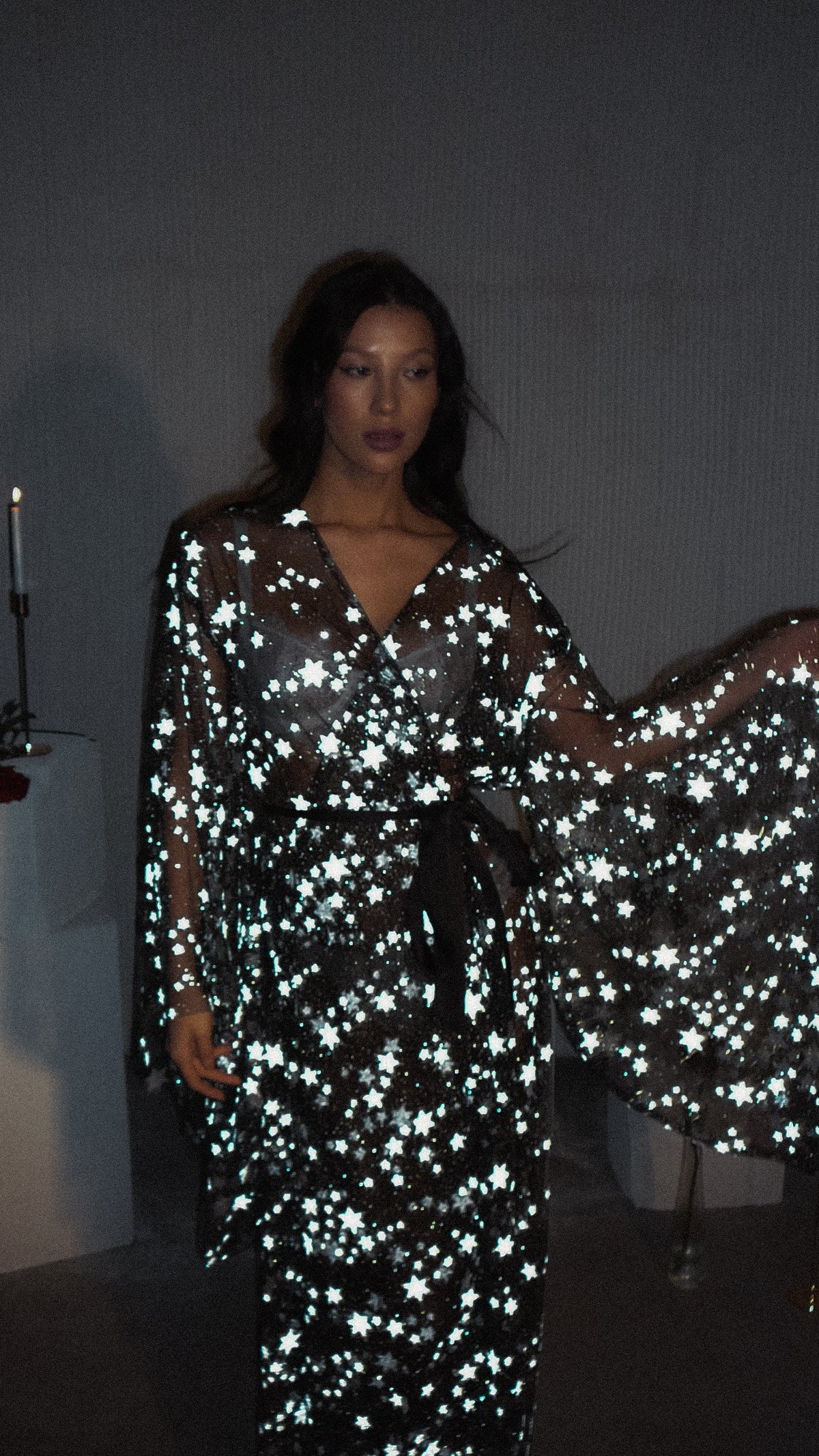 Moody flash shot of a black star bridal robe with bell sleeves spread, model standing in a dark room, Orion Robe Black