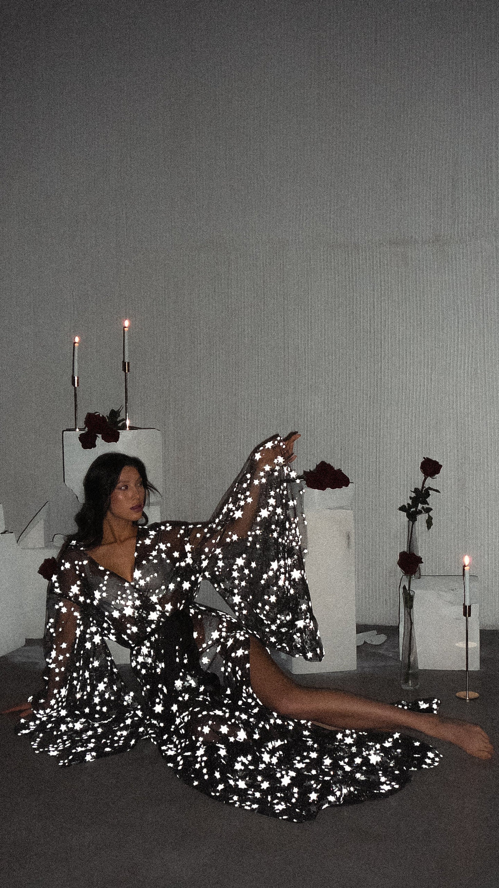 Model reclining on the floor in a black star bridal robe, one sleeve raised, candles and roses behind, Orion Robe Black