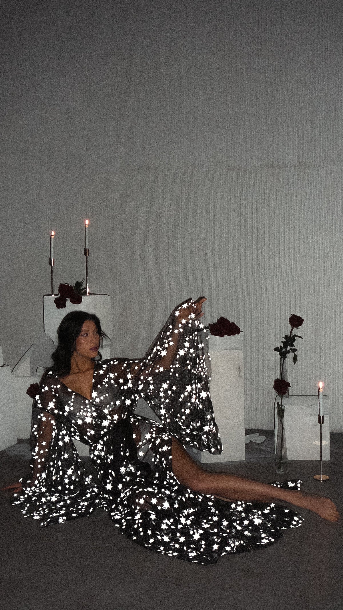Model reclining on the floor in a black star bridal robe, one sleeve raised, candles and roses behind, Orion Robe Black