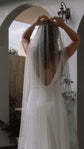 Bride adjusting a pearl cathedral wedding veil at the crown, back view under a white arch, Pearl Cascade Veil