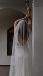 Long pearl wedding veil falling over a low cowl back, bride reaching up against a white archway, Pearl Cascade Veil