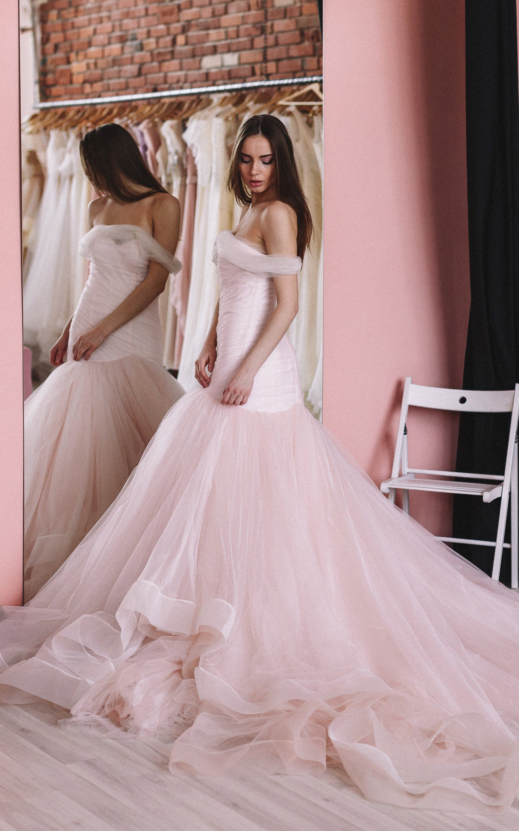 Bride beside a mirror in a fitting room, blush tulle wedding dress with off-shoulder bodice and wide train, Peony