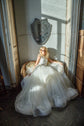 Ivory two-piece wedding dress with a full tulle skirt pooled around a bride seated in a wicker chair, sunlight, Ready or Not Ivory