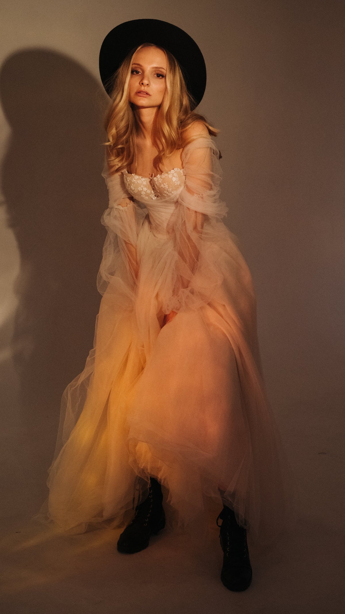 Off-shoulder tulle ball gown wedding dress with puff sleeves and cotton flowers on the corset, bride in a wide hat and boots, Savanna by Ephemeris